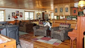 A cozy living room with a fireplace, wooden floors, and a dining area with a kitchen in the background. - The Old Bear BnB (Pine Mountain Club)