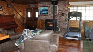 A cozy living room with a fireplace, a treadmill, and a staircase. - The Old Bear BnB (Pine Mountain Club)