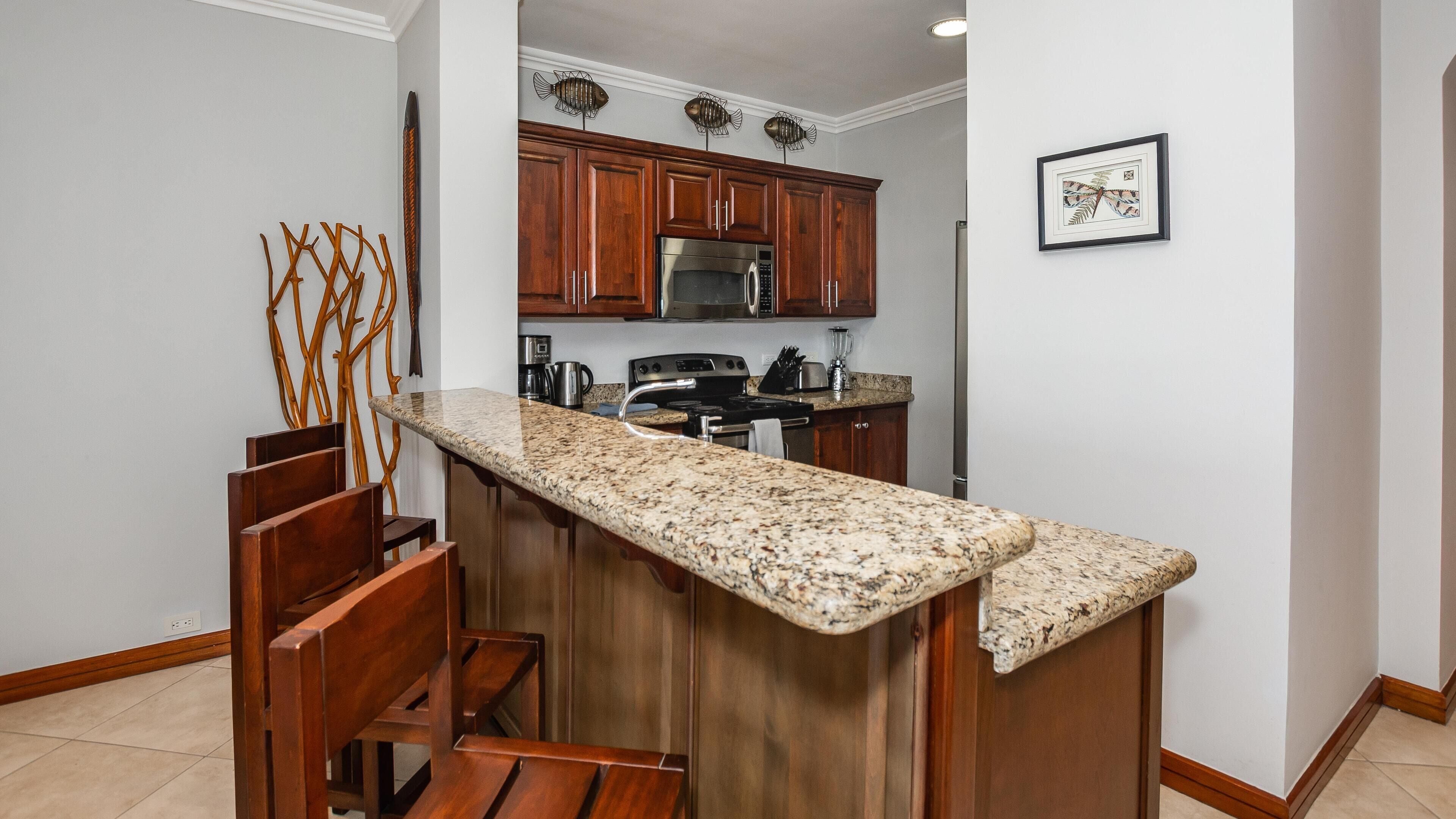 A kitchen with wooden cabinets, a granite countertop, and a stainless steel refrigerator.