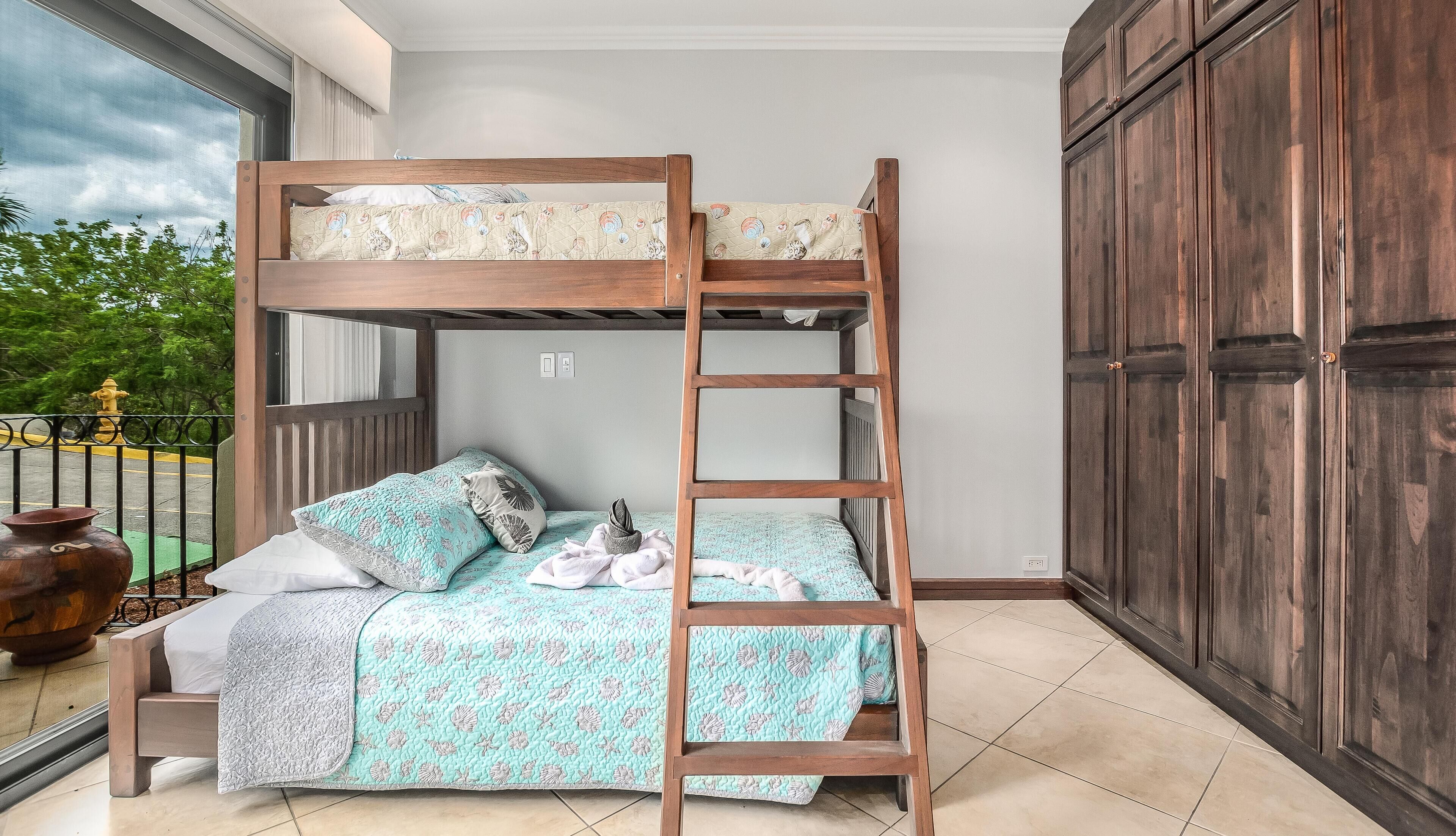 A bunk bed with a ladder, a window with curtains, and a view of trees and a yellow fire hydrant outside.