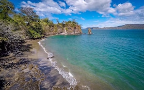 Uma praia com águas turquesa cristalinas, costa rochosa e vegetação exuberante.