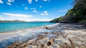 Una playa con aguas azul turquesa, costa rocosa y montañas a lo lejos.