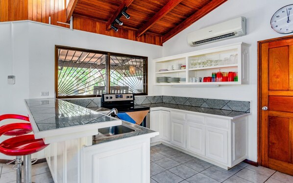 A kitchen with white cabinets, a stove, a sink, and a window with a view of greenery.