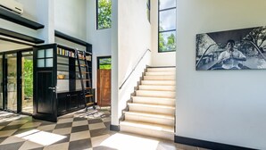 A modern interior with a staircase, a bookshelf, and a painting. - Nostalgic Retro Home on Luxurious Lot with a Private Infinity Pool and Ocean Views (Tempate)