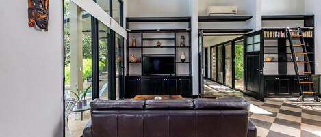 A modern living room with a leather sofa, a flat-screen TV, and a bookshelf.