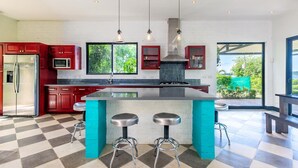 A modern kitchen with a central island, red cabinets, and a checkered floor. - Nostalgic Retro Home on Luxurious Lot with a Private Infinity Pool and Ocean Views (Tempate)