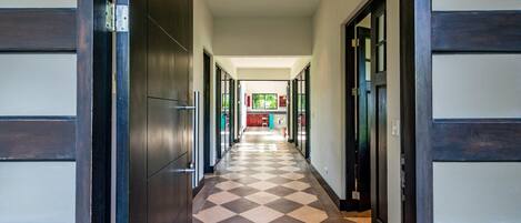 A hallway with a checkered floor, leading to a kitchen area with red cabinets and a window.