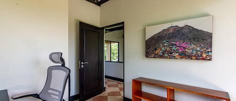 A hallway with a chair, a wooden bench, and a painting of a colorful mountain village.