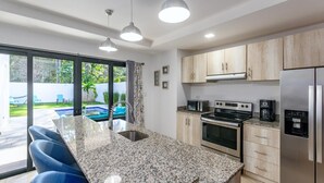 A modern kitchen with granite countertops, stainless steel appliances, and a large island with bar stools. - Ultramodern Townhome with an Inviting Coastal Design and Lush Outdoor Oasis with a Private Pool (Tempate)