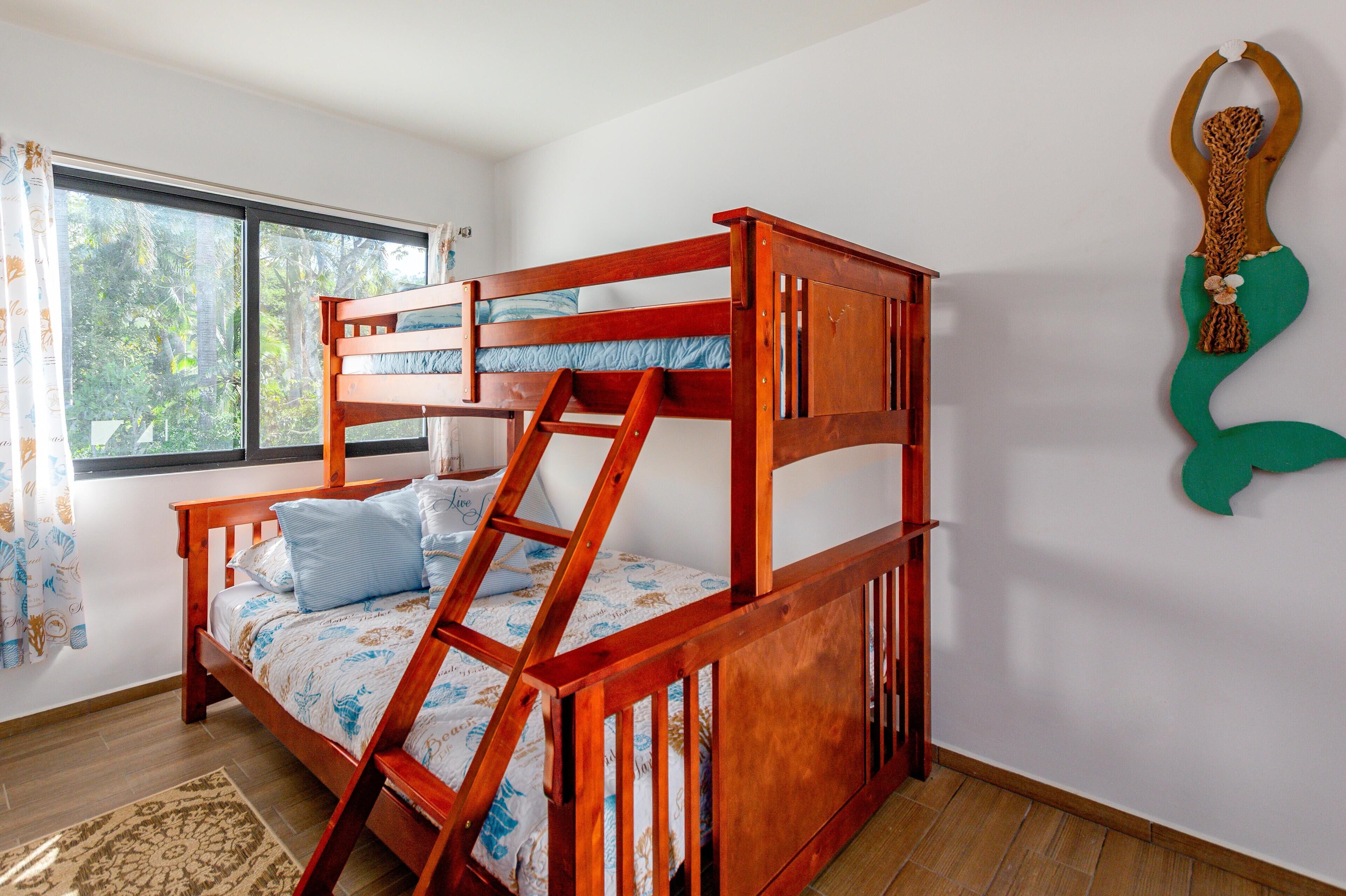 A bunk bed with a ladder, a window with curtains, and a wall decoration.