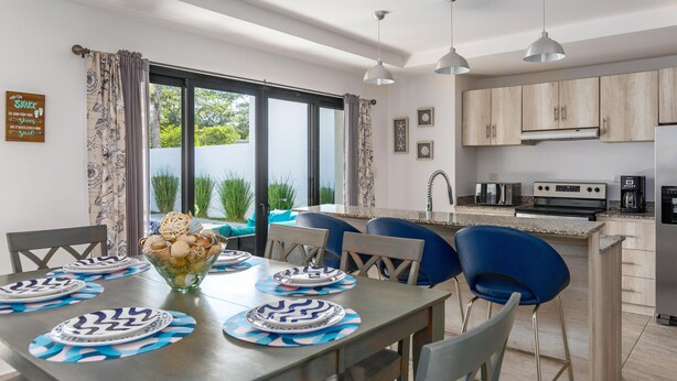 A modern kitchen with a dining area, featuring a large window, a built-in oven, and a coffee machine. - Ultramodern Townhome with an Inviting Coastal Design and Lush Outdoor Oasis with a Private Pool (Tempate)