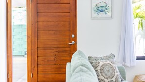 A wooden door with a glass panel, a patterned cushion on a couch, and a framed picture on the wall. - Ultramodern Townhome with an Inviting Coastal Design and Lush Outdoor Oasis with a Private Pool (Tempate)