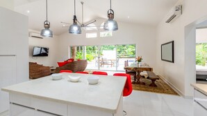 A modern kitchen with a central island, a dining area with red chairs, and a TV mounted on the wall. - Modern Home and Guesthouse in a Peaceful Gated Community with a Private Swimming Poo (Cabo Velas)