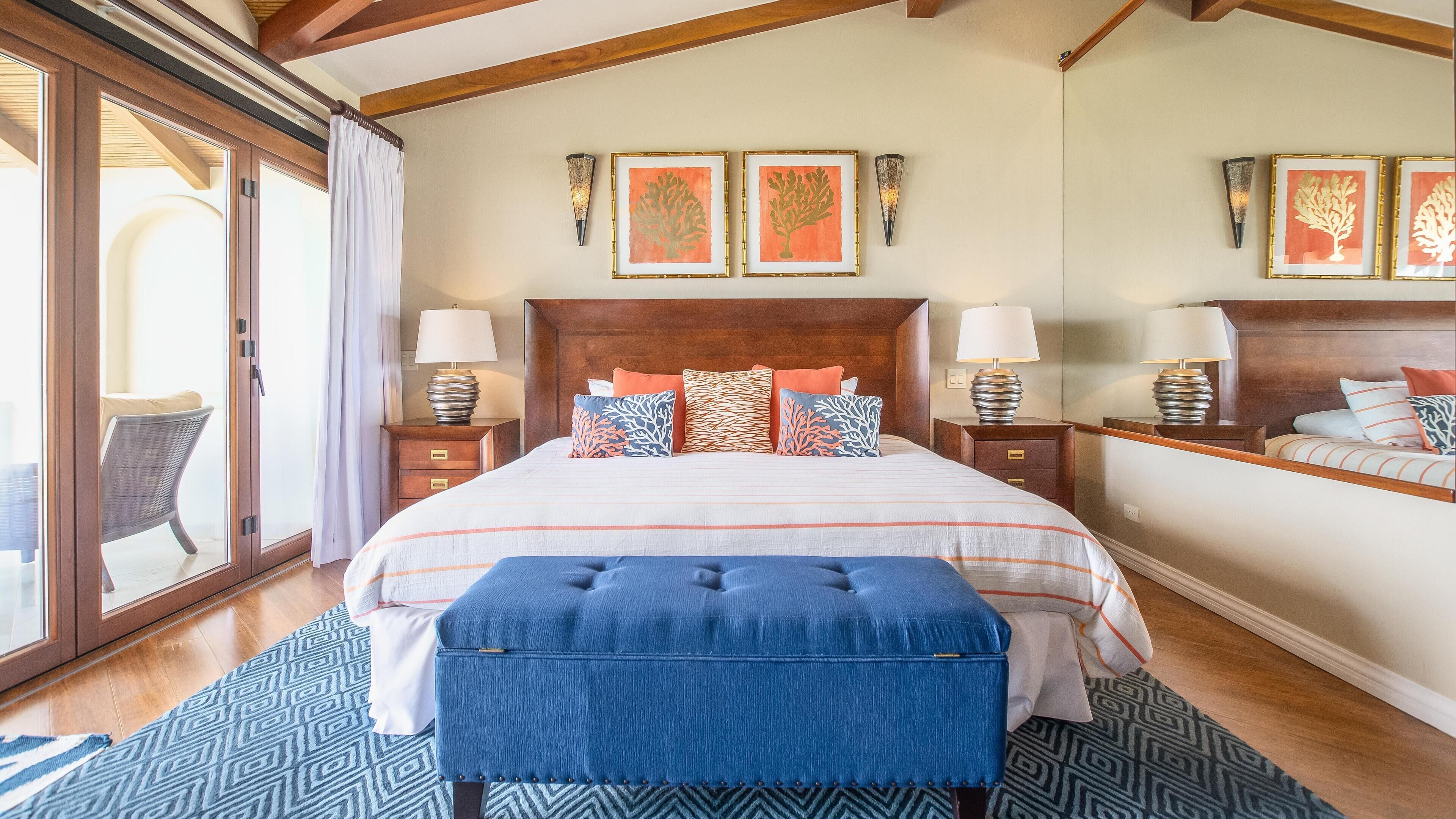 A bedroom with a large bed, two bedside tables with lamps, a wooden headboard, and a large window with curtains.