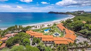 Um resort costeiro com praia, piscina e vegetação exuberante.