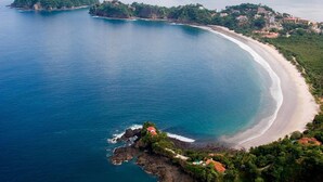 An aerial view of a coastal area with a curved beach, rocky outcrops, and scattered buildings. - Luxury Ocean-View Flamingo Home with Pool, Apartment and Party Deck (Cabo Velas)
