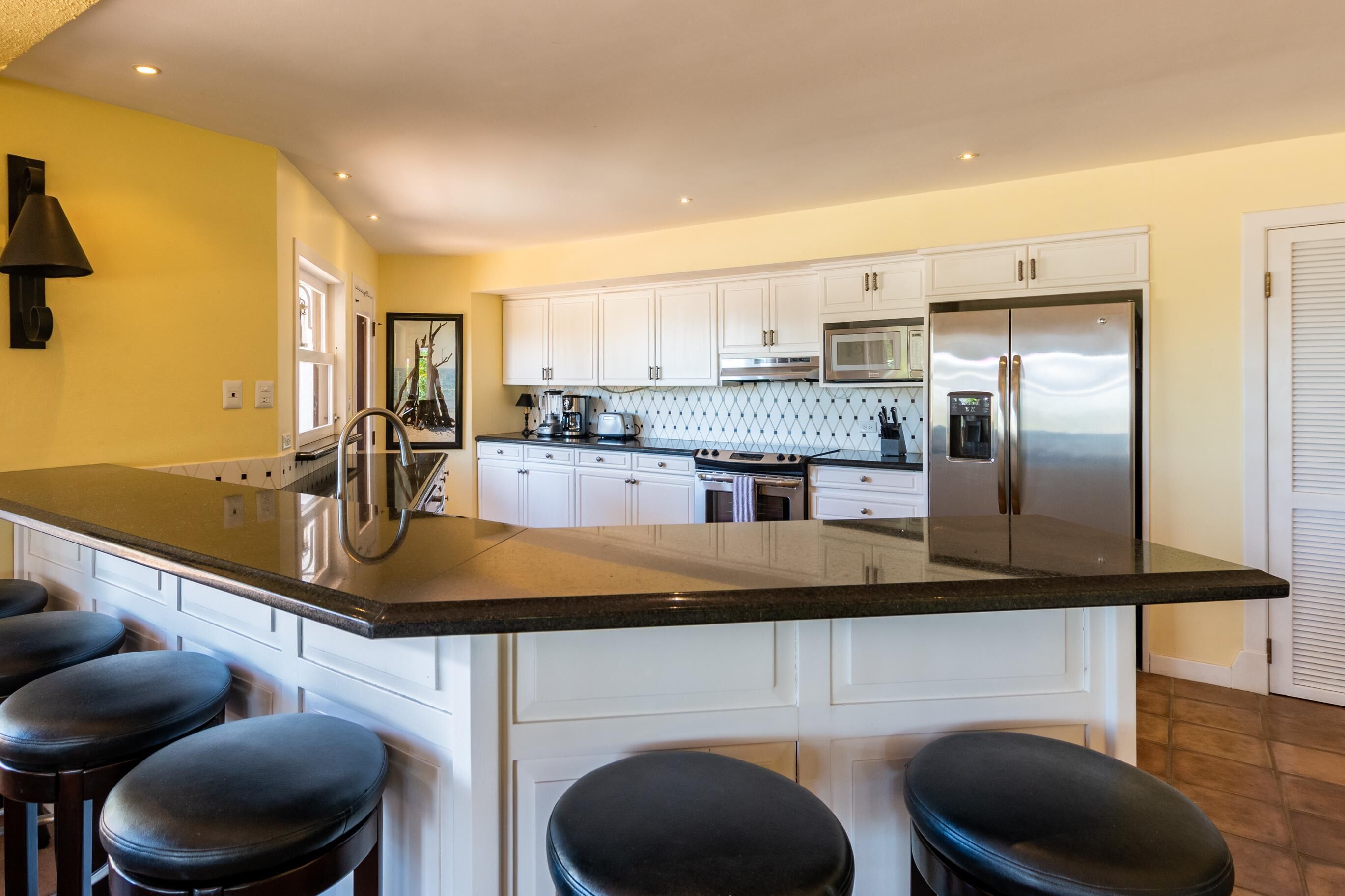 A modern kitchen with white cabinets, a stainless steel refrigerator, and a large island with bar stools.