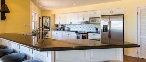 A modern kitchen with white cabinets, a stainless steel refrigerator, and a large island with bar stools.