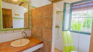 Een badkamer met een wastafel, spiegel, douche en raam.