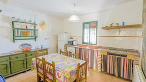 A kitchen with a dining table, green cabinets, a hanging light fixture, and a window with blinds.