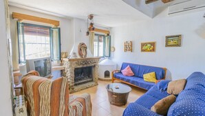 A living room with a stone fireplace, a blue sofa, and a television. - El Garrotal - El Pan El Bosque by Ruralidays (Cádiz)