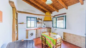 Een kleine keuken met een wasmachine, een eettafel met een kleurrijke tafelkleed en een houten plafond.