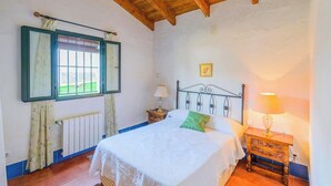 Een slaapkamer met een bed, twee nachtkastjes, een raam met gordijnen, een radiator en een houten plafond.