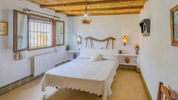 Een slaapkamer met een bed, een radiator, een raam met tralies, een houten plafond en wandlampen.