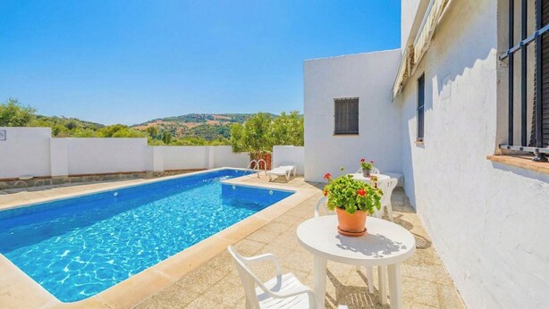 Une piscine rectangulaire avec un mur extérieur blanc, une petite fenêtre et une table blanche sur laquelle est posée une plante en pot.