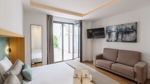 A hotel room with a bed, a sofa, a TV, and a sliding glass door to a balcony.