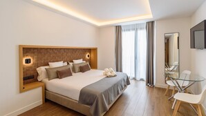 Una habitación de hotel moderna con una cama grande, mesitas de noche, una mesa de vidrio con sillas, un espejo y un televisor.