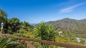 Een mooi uitzicht vanaf een balkon met houten reling, uitkijkend over een bergachtig landschap en een kronkelende weg.