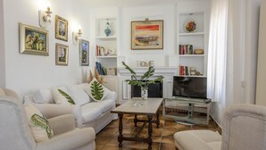 Een woonkamer met een bank, salontafel, televisie en boekenplanken met boeken en decoratieve objecten.