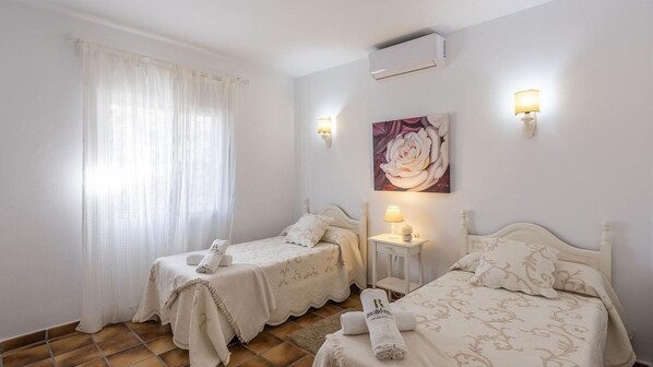 Una camera da letto con due letti singoli, un comodino con una lampada, un quadro di una rosa e un condizionatore d'aria a parete.