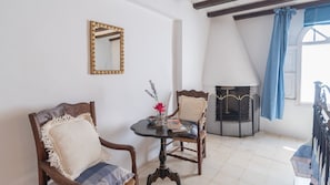 A room with two wooden chairs, a small round table with a vase of flowers, a fireplace, and a window with blue curtains. - Casa Chantal Gaucín by Ruralidays (Málaga)