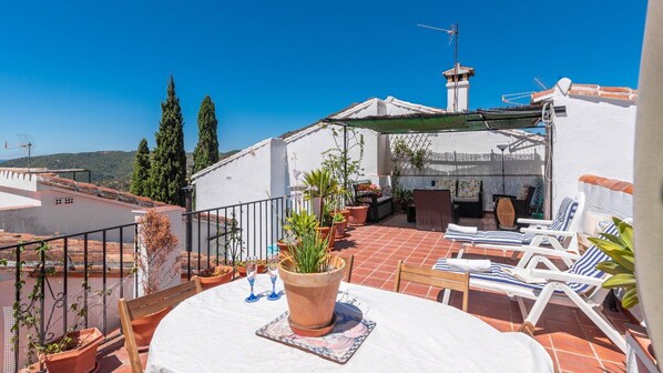 A rooftop terrace with a table, chairs, potted plants, and a view of the landscape.
