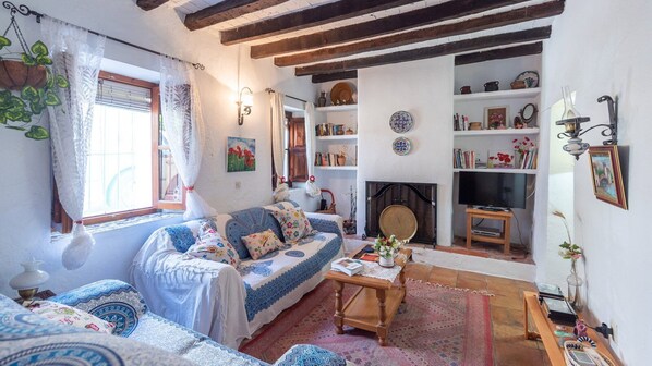 A cozy living room with a sofa, a coffee table, and a fireplace. There are bookshelves and decorative items on the walls. - Casa Chantal Gaucín by Ruralidays (Málaga)