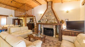 A cozy living room with a stone fireplace, wooden beams, and a television.
