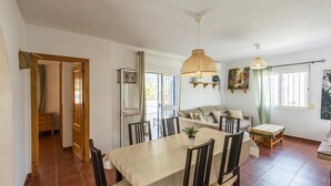 A dining area with a table and chairs, a sofa, and a hanging light fixture.