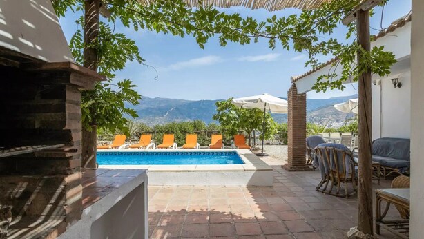 A pool area with a view of mountains, outdoor seating, and a barbecue grill.