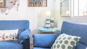 Een kamer met twee blauwe fauteuils, een kleine ronde tafel met een lamp, en een wandplank met decoratieve objecten.