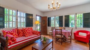 Um quarto com um sofá vermelho, uma mesa de jantar com cadeiras e um candelabro.