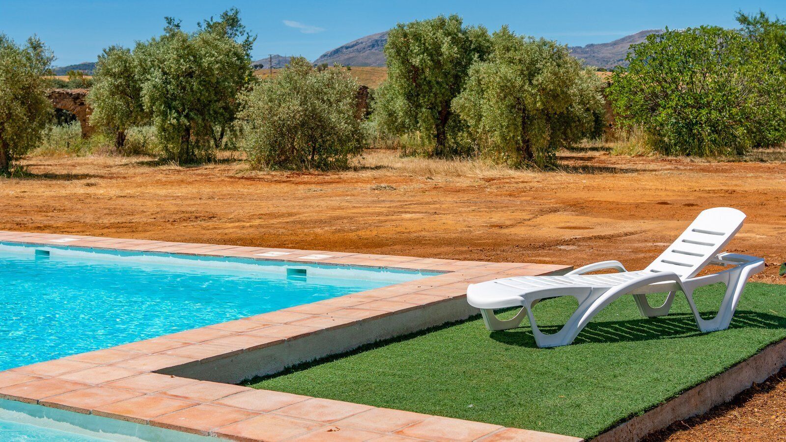 A swimming pool with a white lounge chair and artificial grass edging.