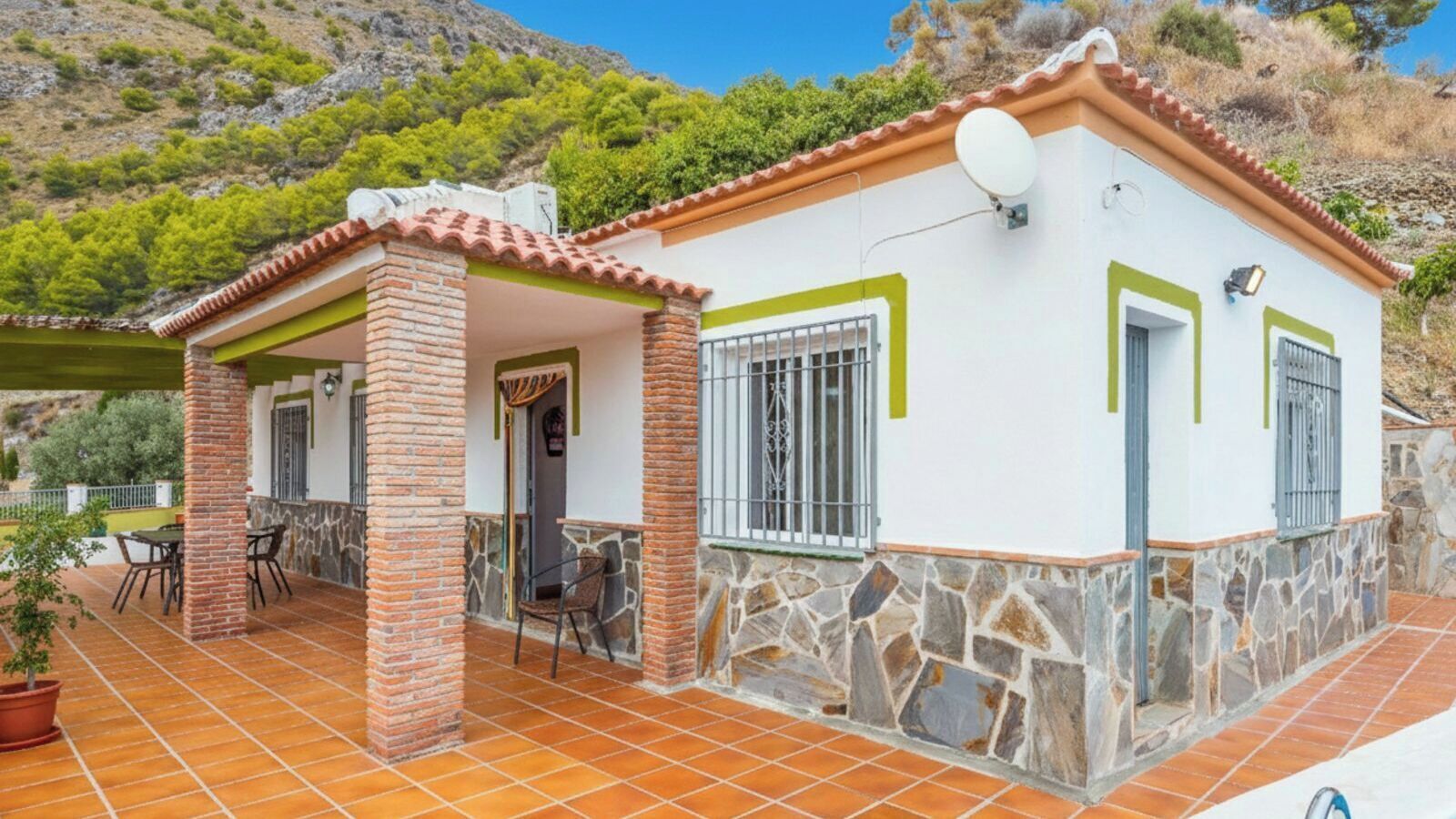A two-story house with a patio, stone walls, and a satellite dish.