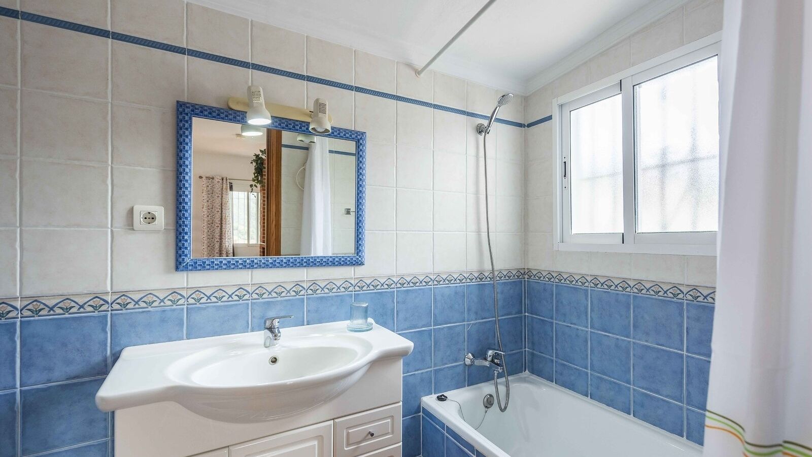 Une salle de bain avec un lavabo, un miroir, une douche et une fenêtre.