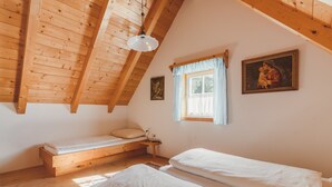 A cozy attic bedroom with wooden beams, a sloped ceiling, a single window with curtains, a bed, and a small table. - Alpin Cabin in Klippitz (Klippitztörl)