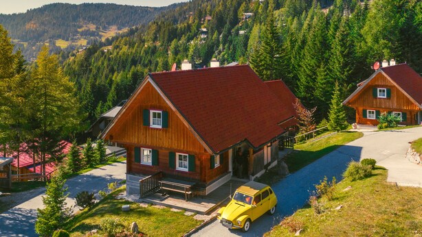 A wooden cabin with a red roof, a small porch, and a yellow car parked in front. - Alpin Cabin in Klippitz (Klippitztörl)