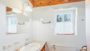 A bathroom with a white sink, wooden vanity, a mirror with lights, a window with a view of trees, and a white radiator. - Alpin Cabin in Klippitz (Klippitztörl)