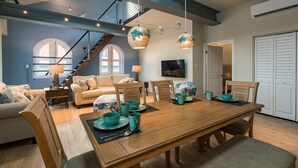 Amplia sala de estar con una mesa de comedor de madera dispuesta para cuatro personas, una escalera y un gran ventanal con vistas.