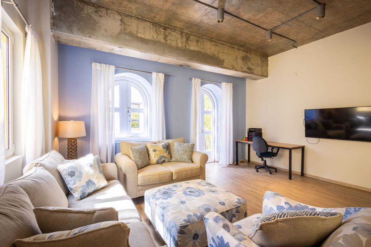 A living room with a sofa, ottoman, and a flat-screen TV mounted on the wall.